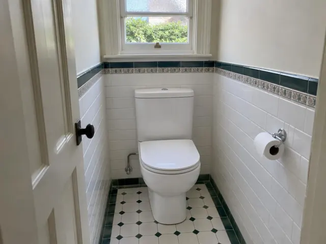 Clean white toilet in a tiled small bathroom with a window in Rose Bay
